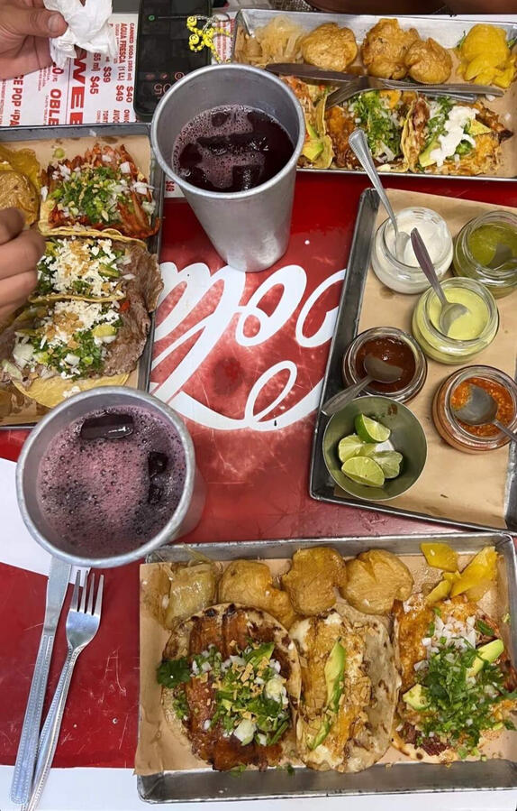 Authentic Taqueria Orinoco Feast vibrant table set with various tacos on metal trays, salsas, and hibiscus water at Taqueria Orinoco,