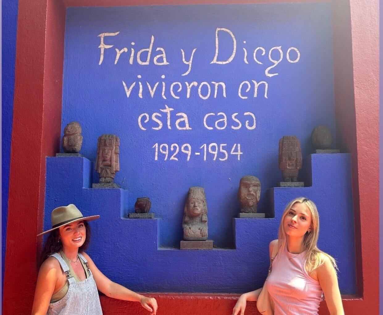 Iconic Art History: Casa Azul Experience Two visitors posing in front of the famous 'Frida y Diego' mural at the Casa Azul in Coyoacán, highlighting the artistic and historical depth of our curated Mexico City tours.